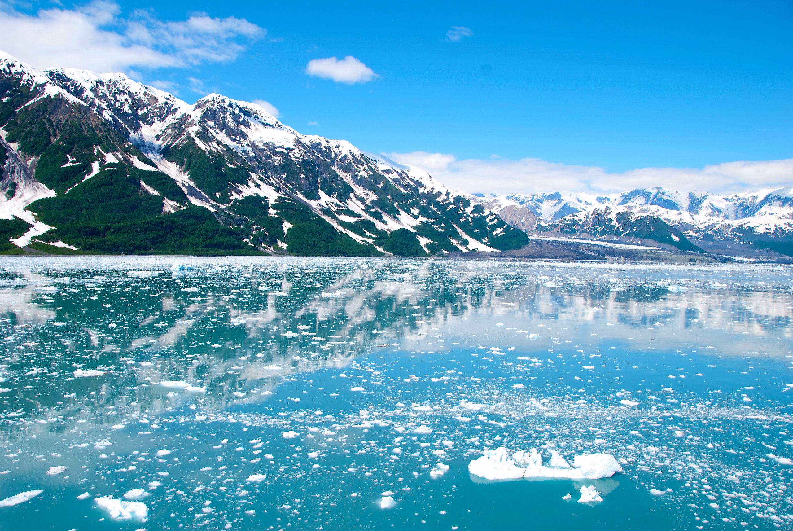 A breathtaking view of Alaskan glaciers reflecting on tranquil icy waters under a clear blue sky.