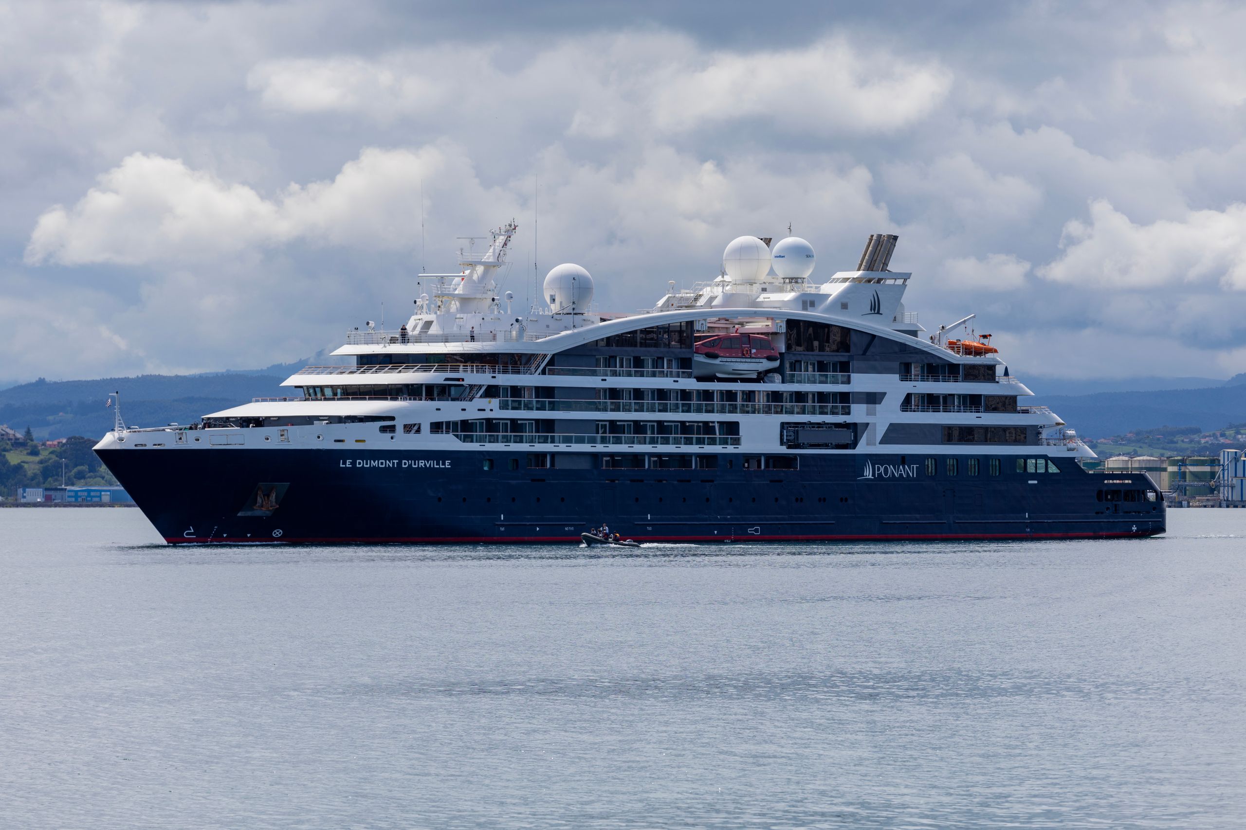 Elegant cruise ship Le Dumont D'Urville sailing on calm waters under cloudy skies.