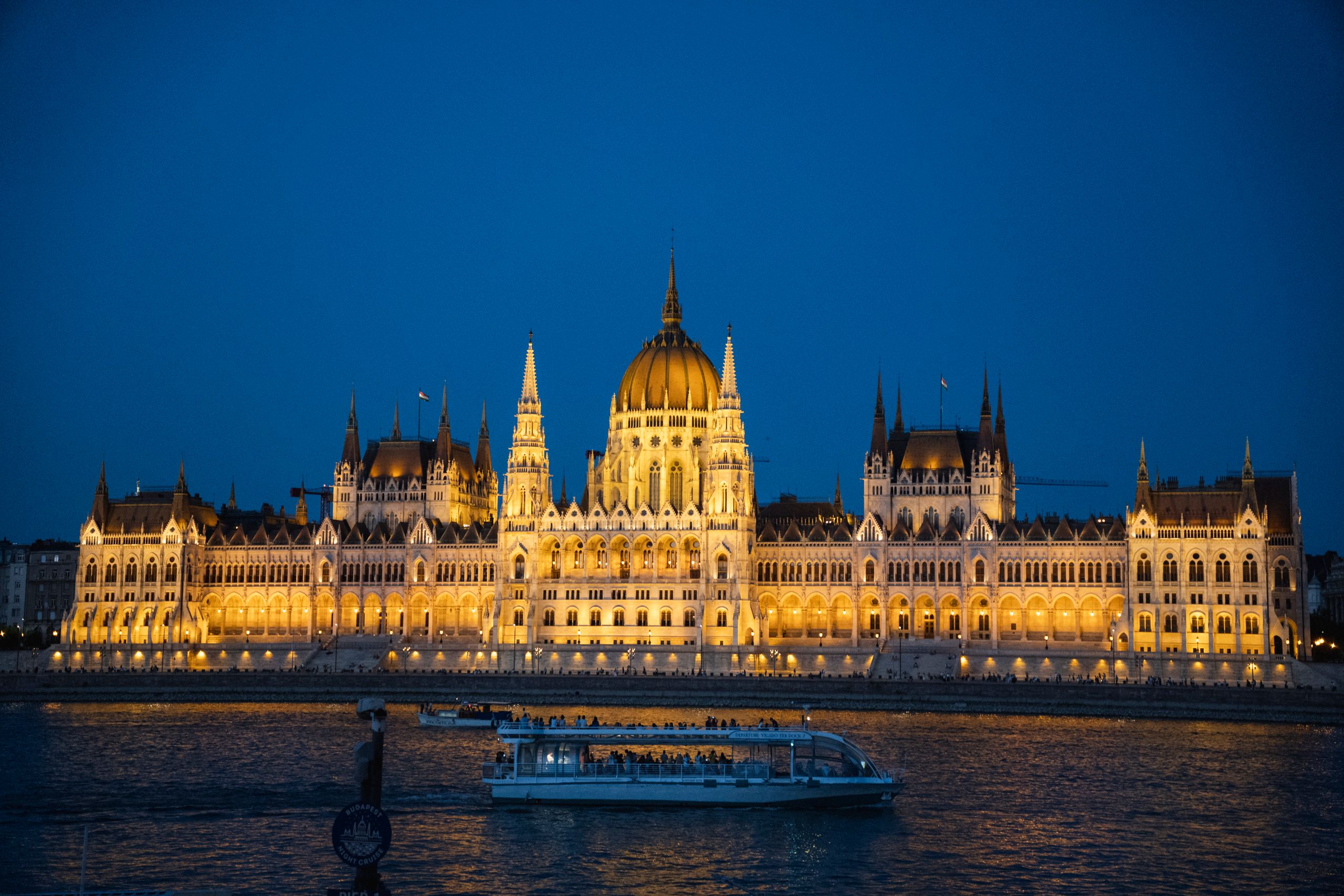 Illuminated Hungarian Parliament Building reflecting on the Danube River at night.